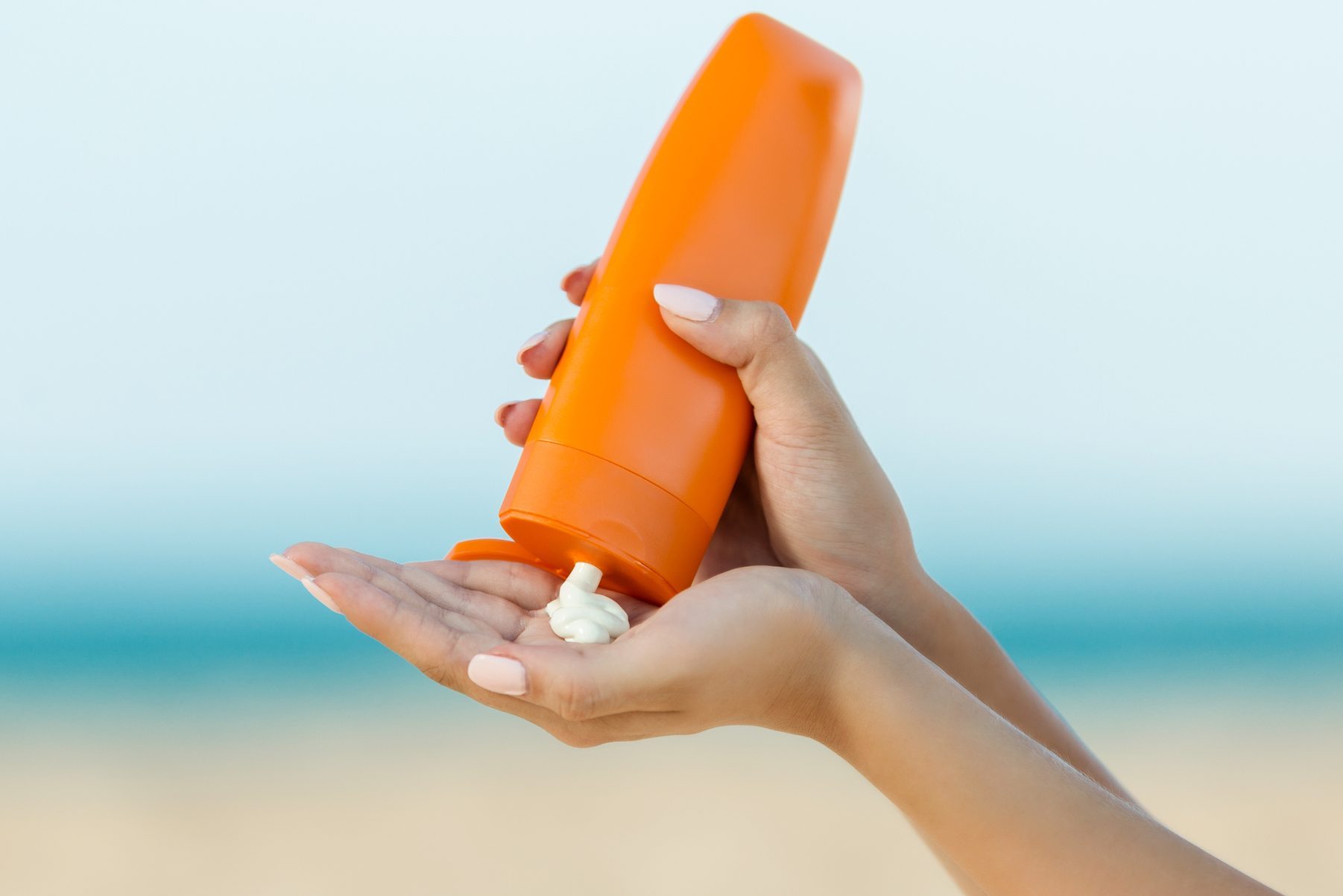 Woman hand apply sunscreen on the beach