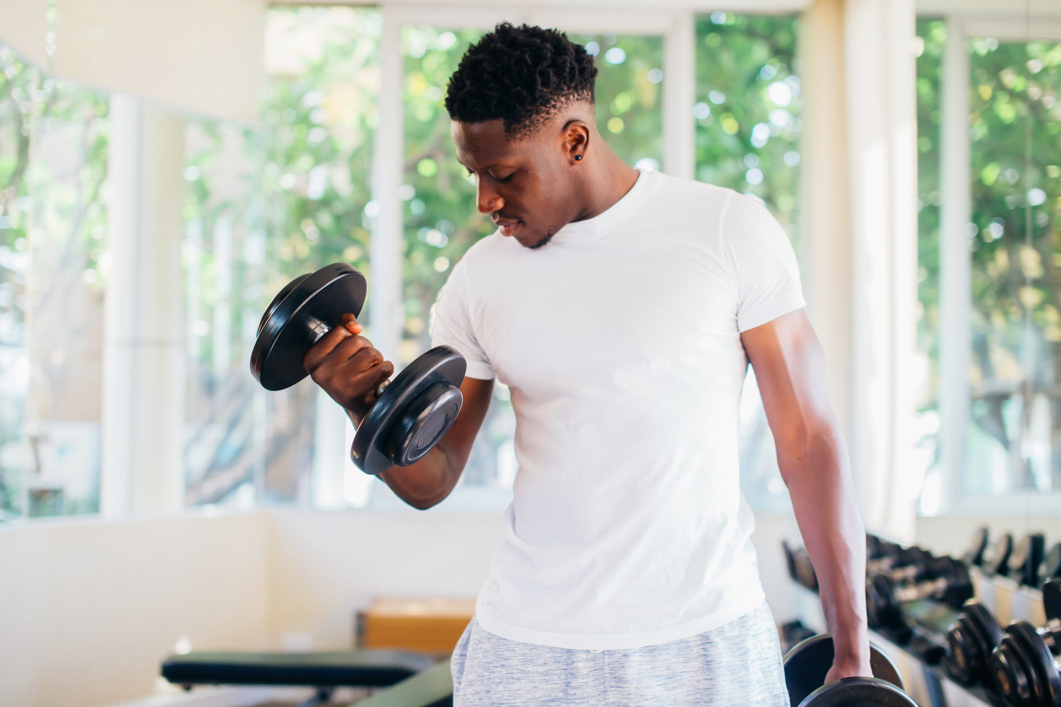 Young African American man standing and lifting a dumbbell with the rack at gym