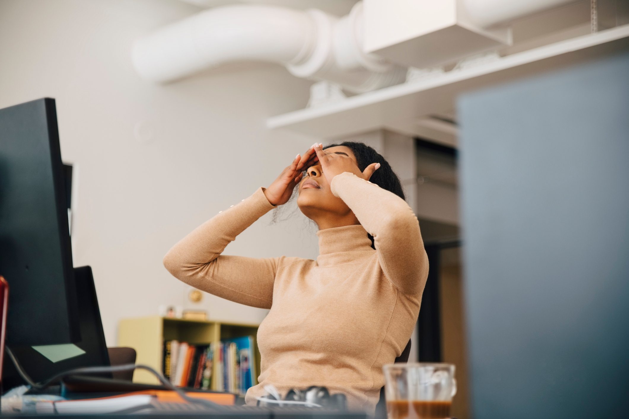 Frustrated female computer programmer with head in hands sitting in creative office