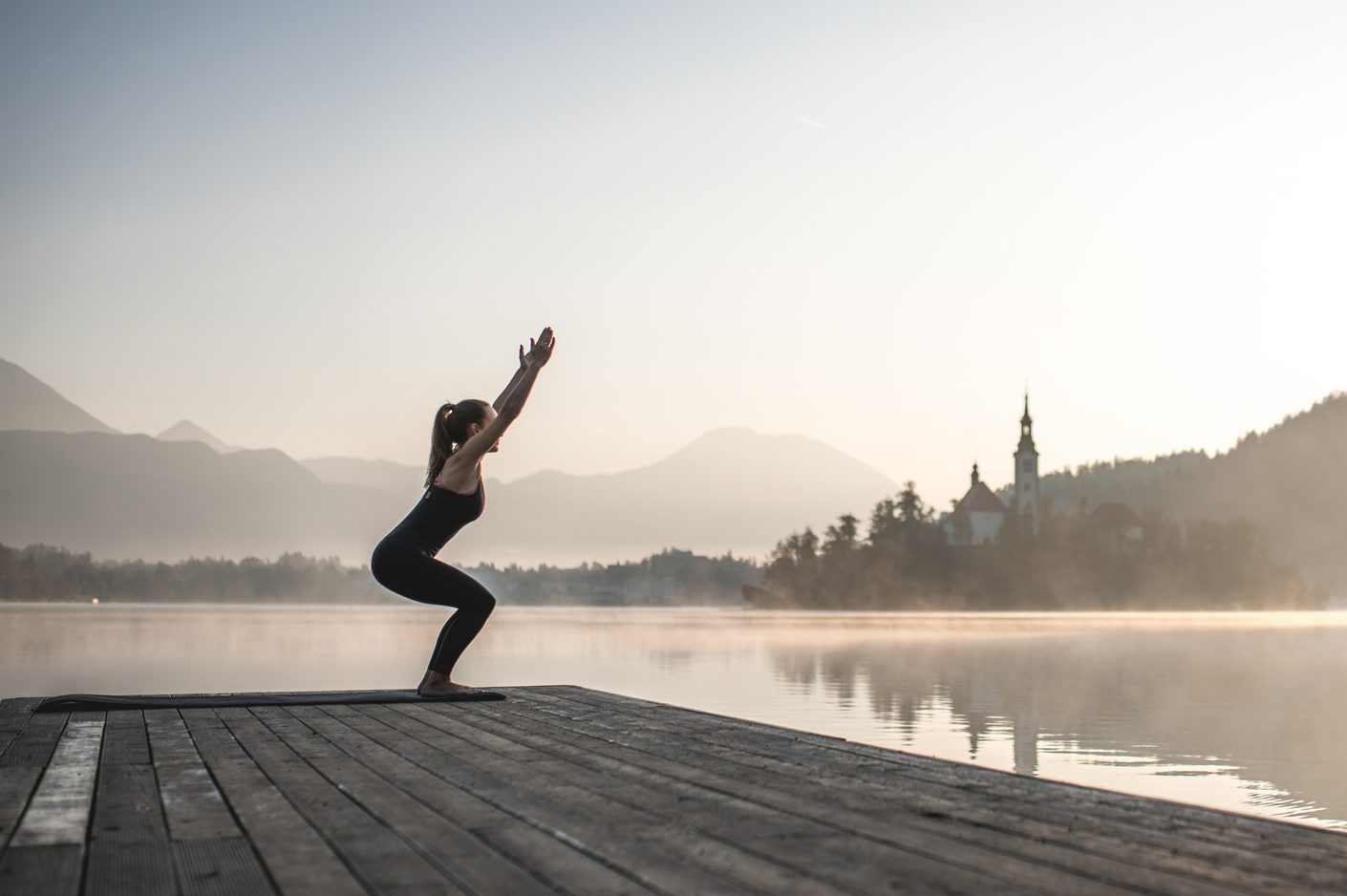 Woman in Yoga Chair Position on Pier Overlooking Lake Bled