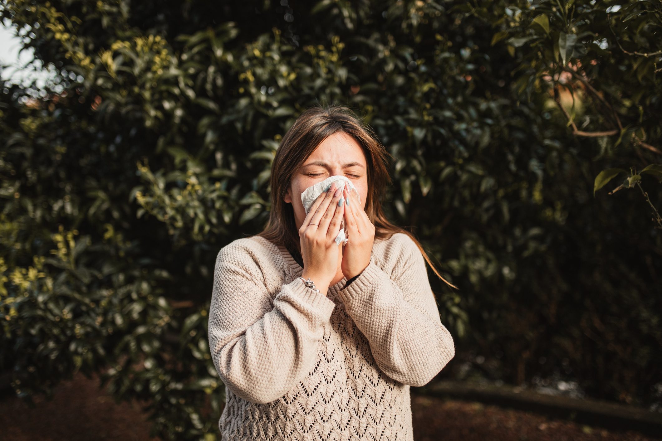 young woman suffering spring allergy and blowing nose with a tissue in the nature