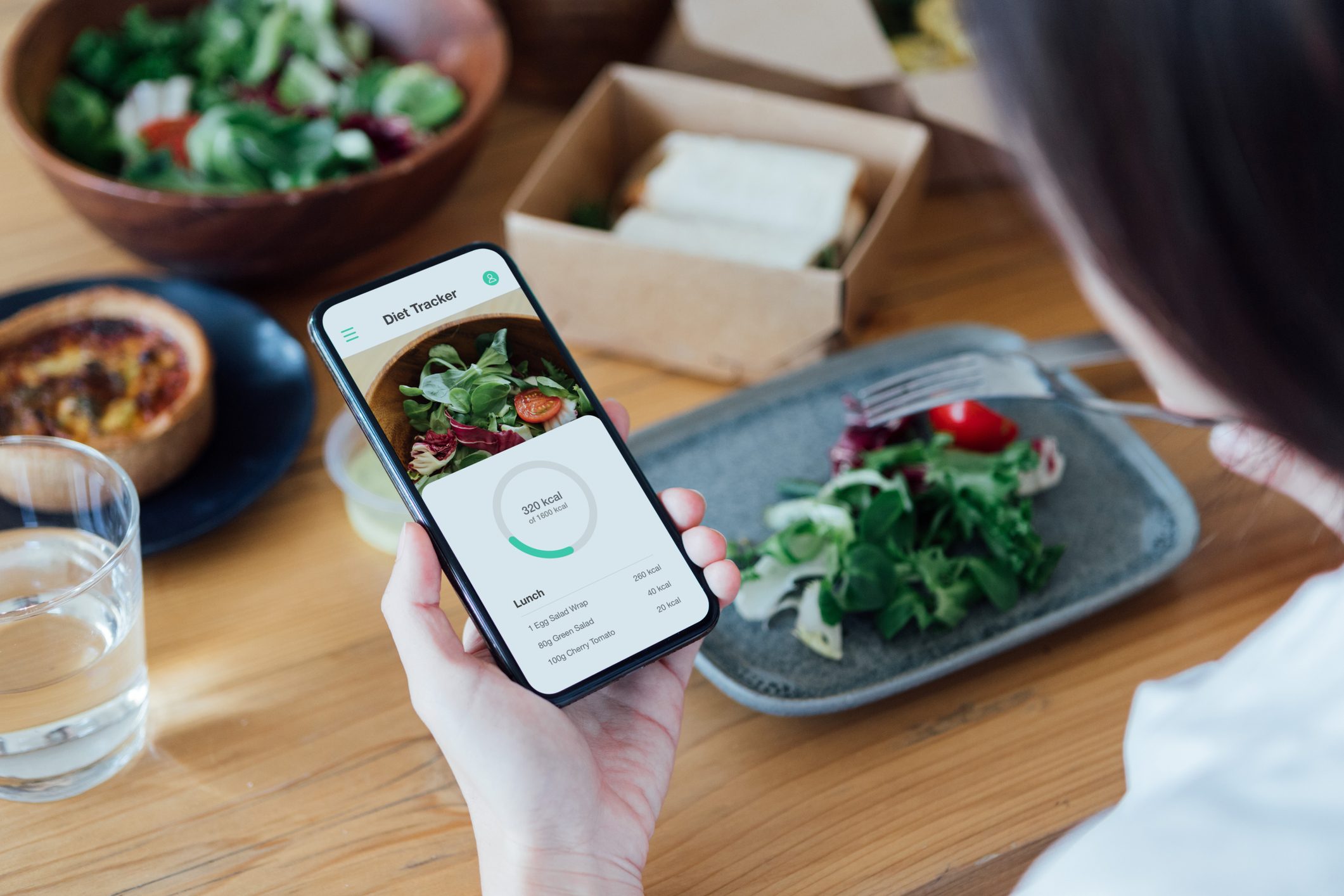 Young Woman Counting Calories With Smartphone While Eating