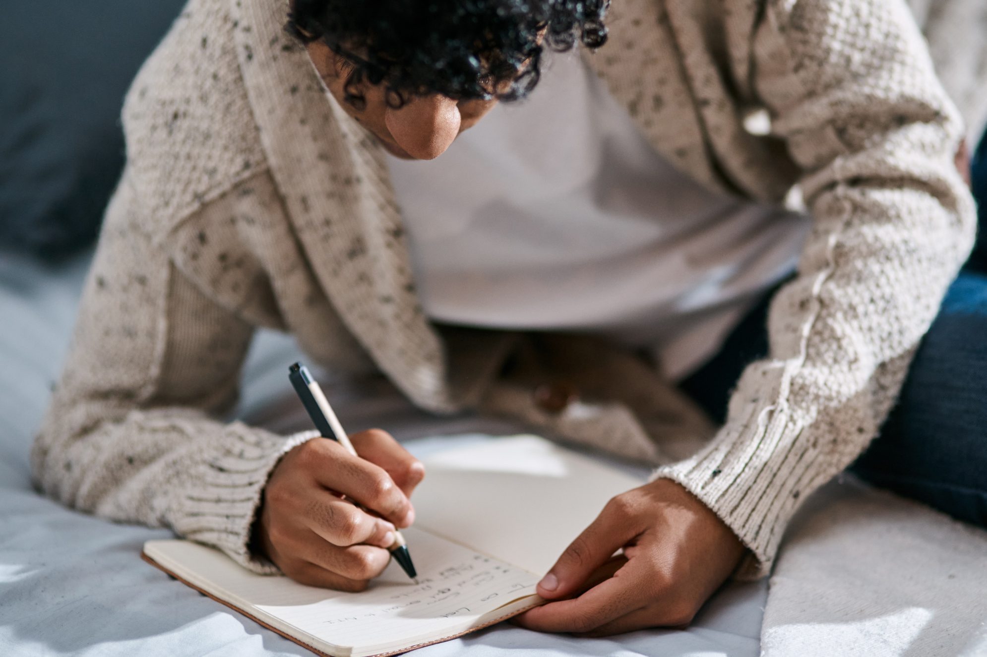 Cropped shot of a man writing in a notebook on his bed at home