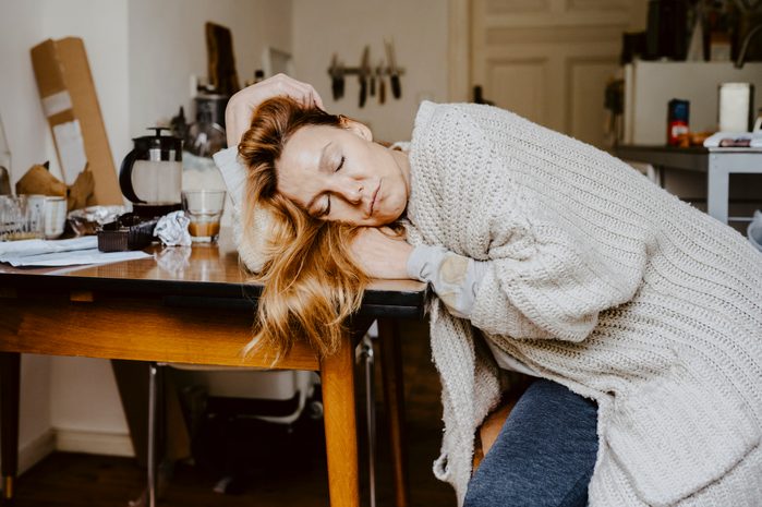 Mature woman with eyes closed on table in living room