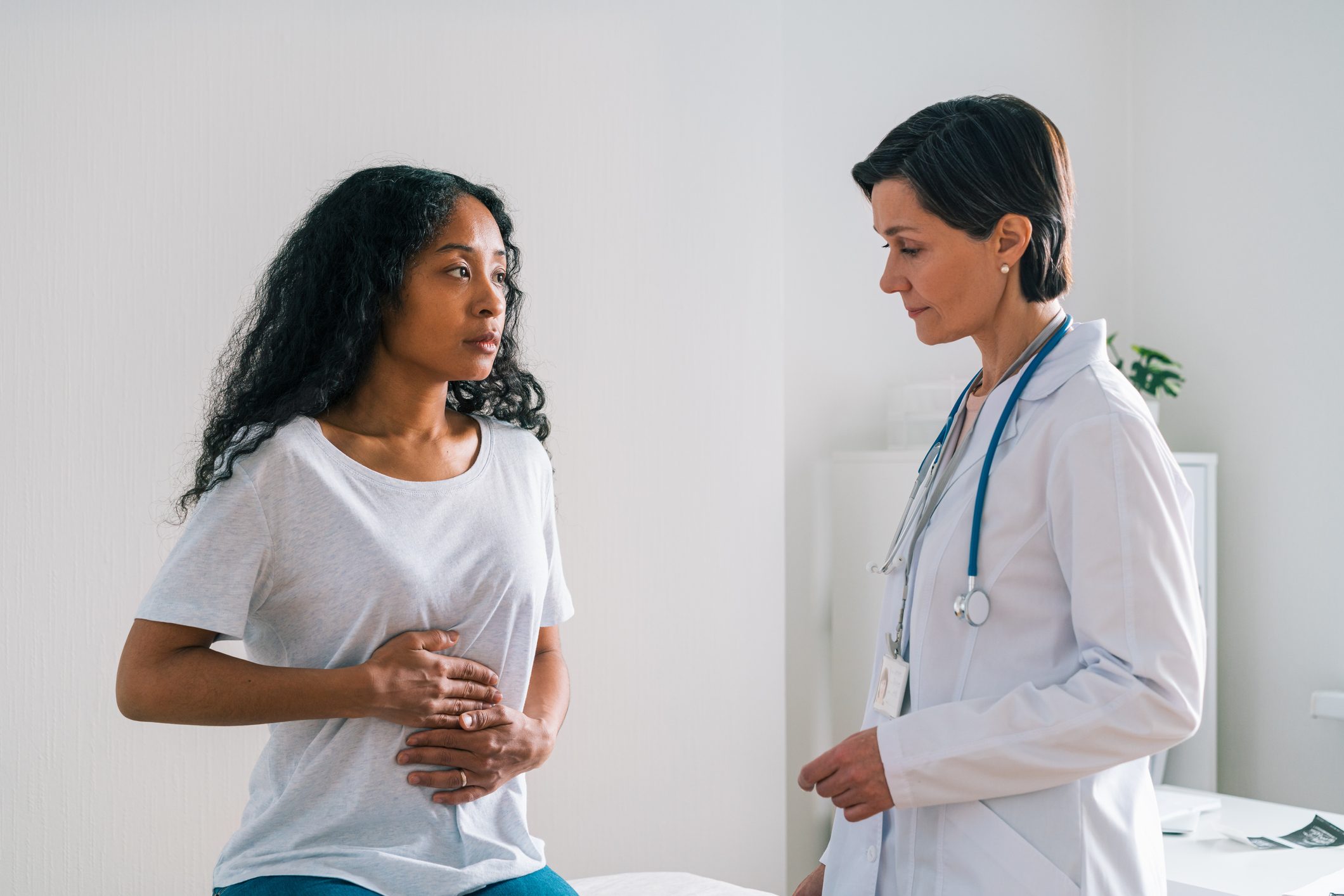 Young African-american patient complaining about belly ache to mature female doctor