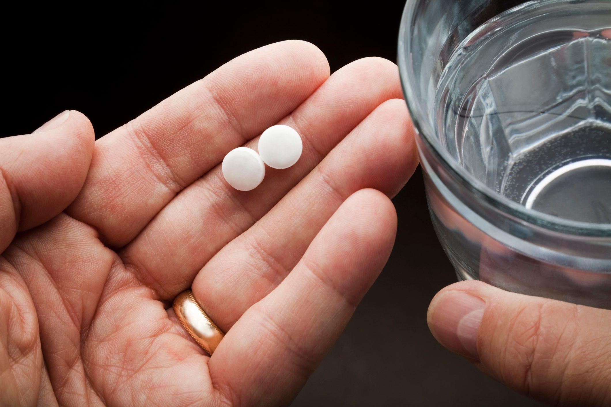 hands holding two aspirin and a glass of water