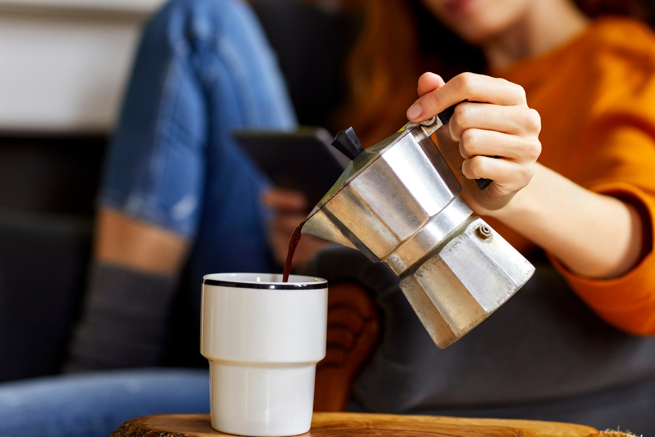 Young woman pouring coffee into cup at home