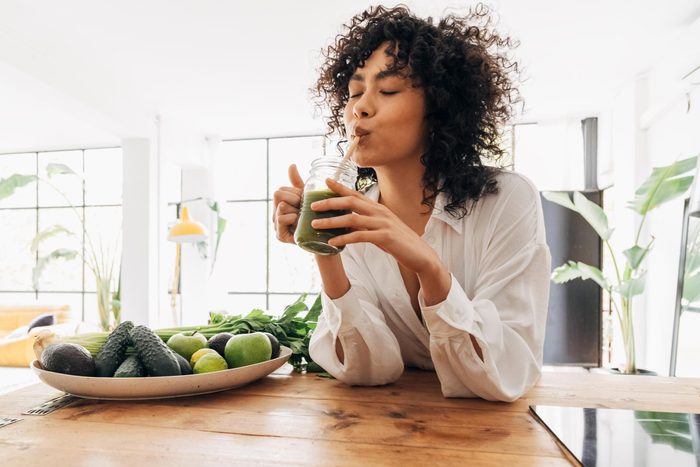 Young african american woman drinking green juice with reusable bamboo straw in loft apartment
