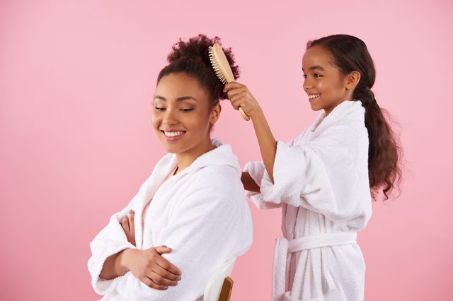 Little African American Girl Is Combing Mother Hair Isolated On Pink Background Studio Portrait