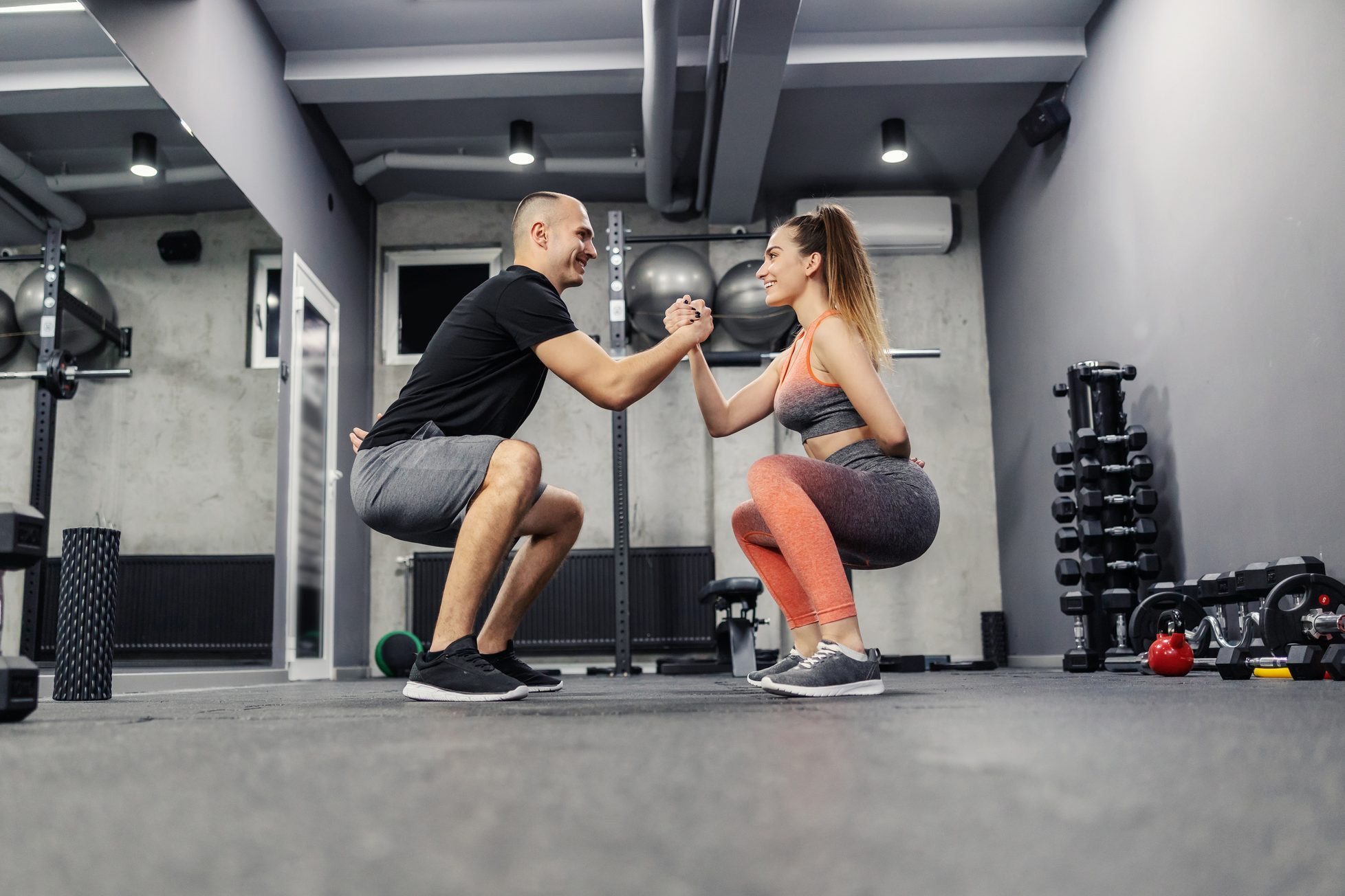 The concept of sports interesting and different fitness training. The couple does sports exercises together. They maintain balance by holding hands and doing squats, couple relationship goal