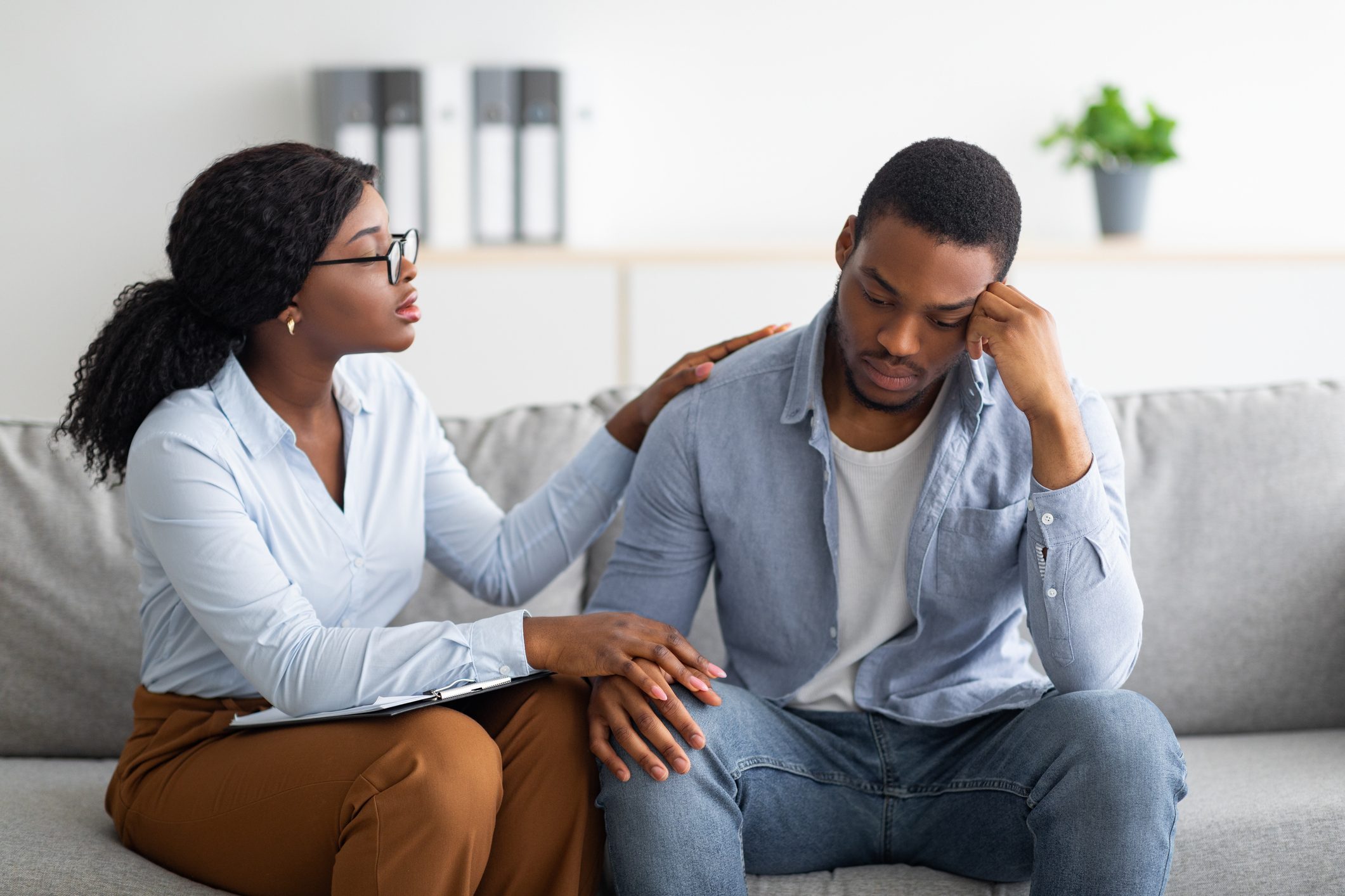 Upset black guy suffering from depression, his counselor supporting him at office