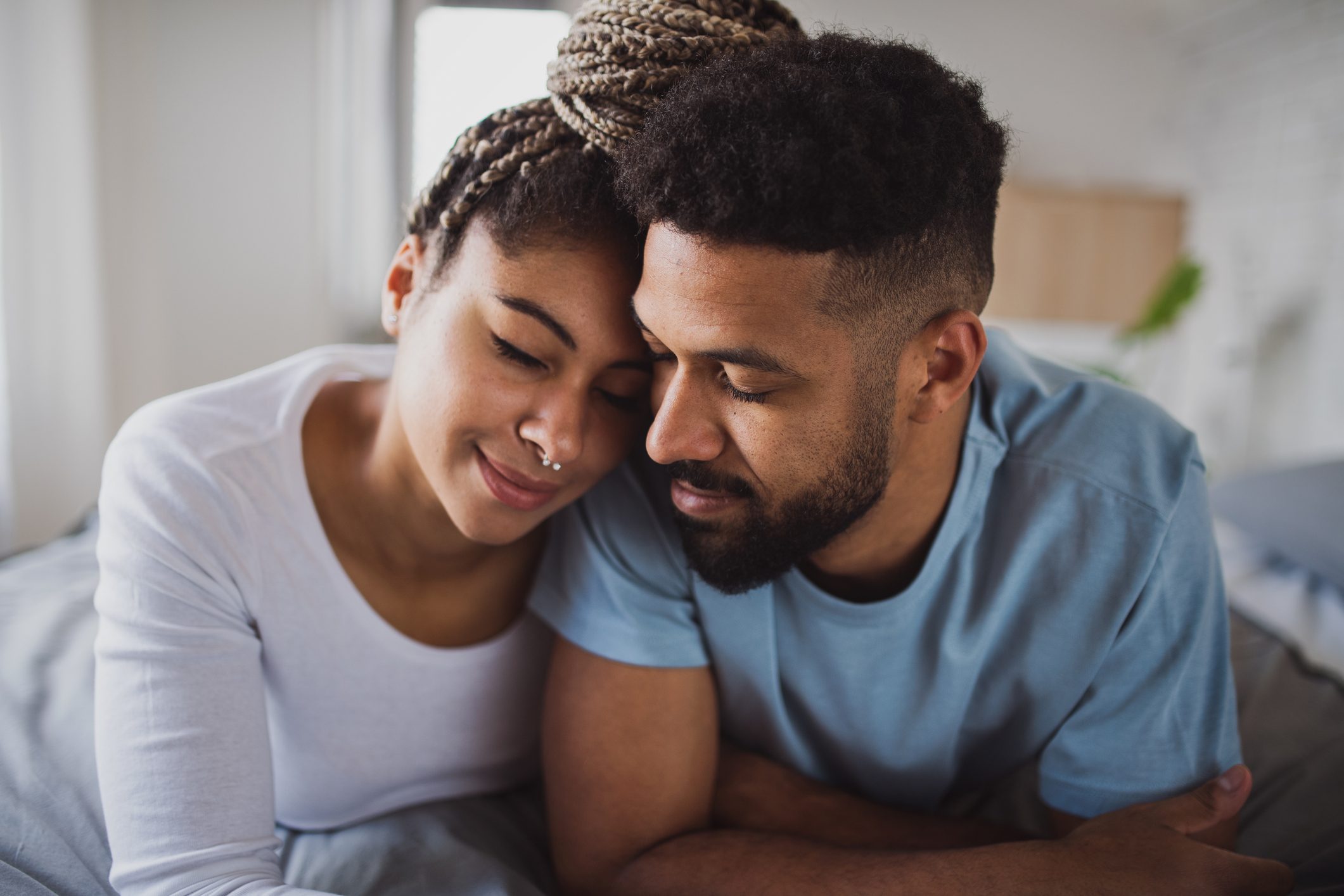 Portrait of young couple on bed indoors at home, cuddling.