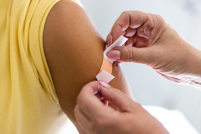 Female doctor hands putting band-aid on woman arm after giving vaccine