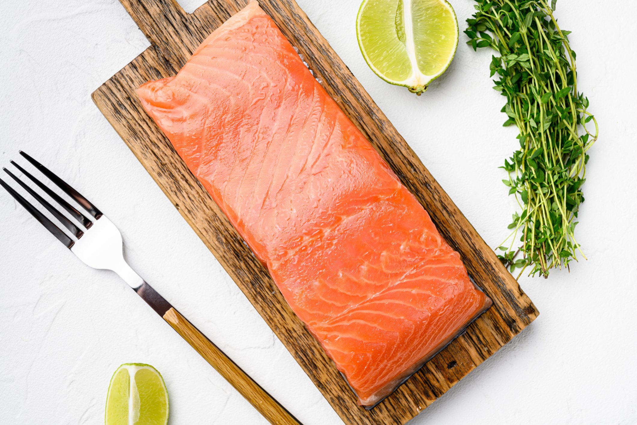 Portioned raw salmon fillet, with herbs, on white stone table background, top view flat lay