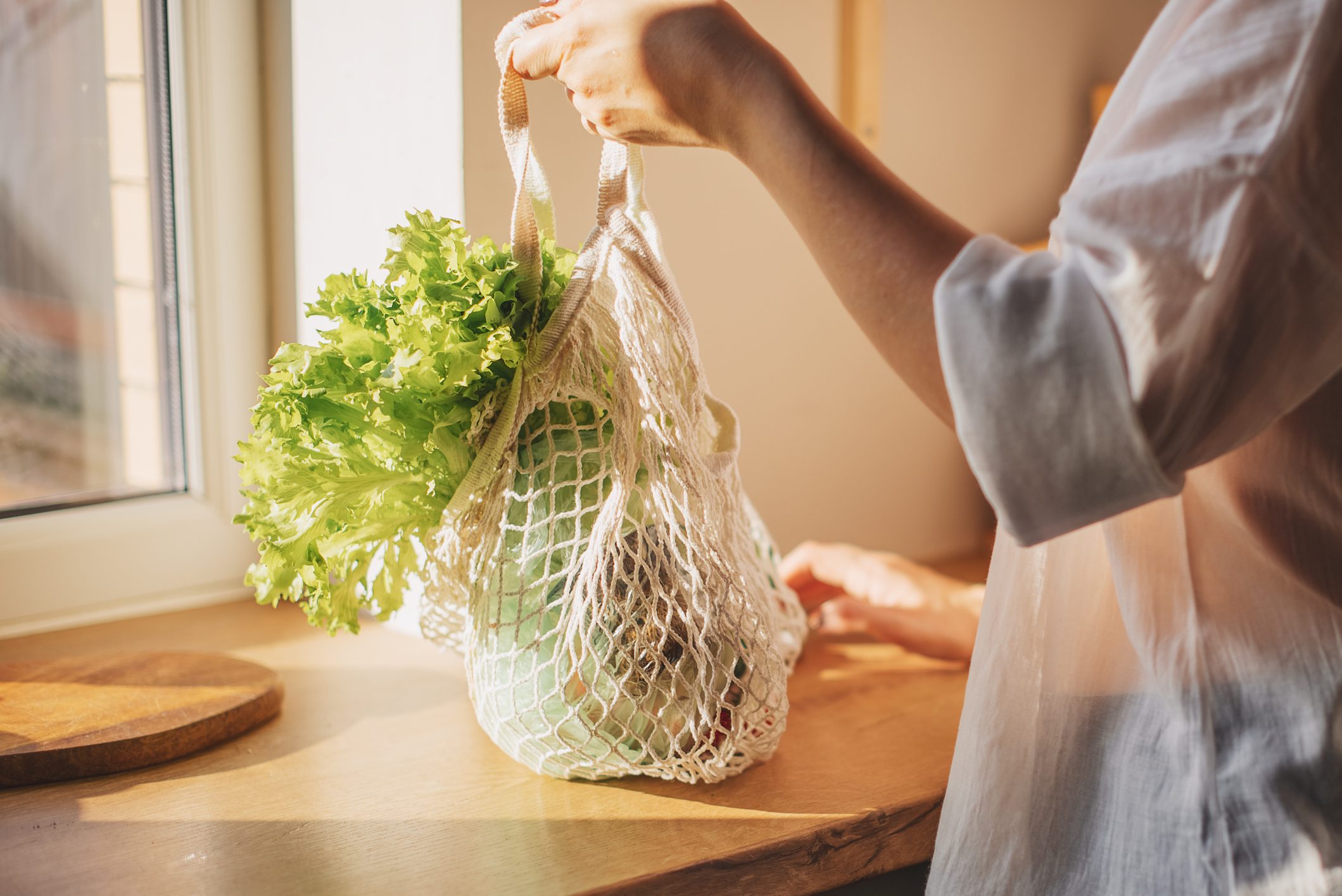 Shopping bag with raw vegetables and fruits held by young woman in casualwear