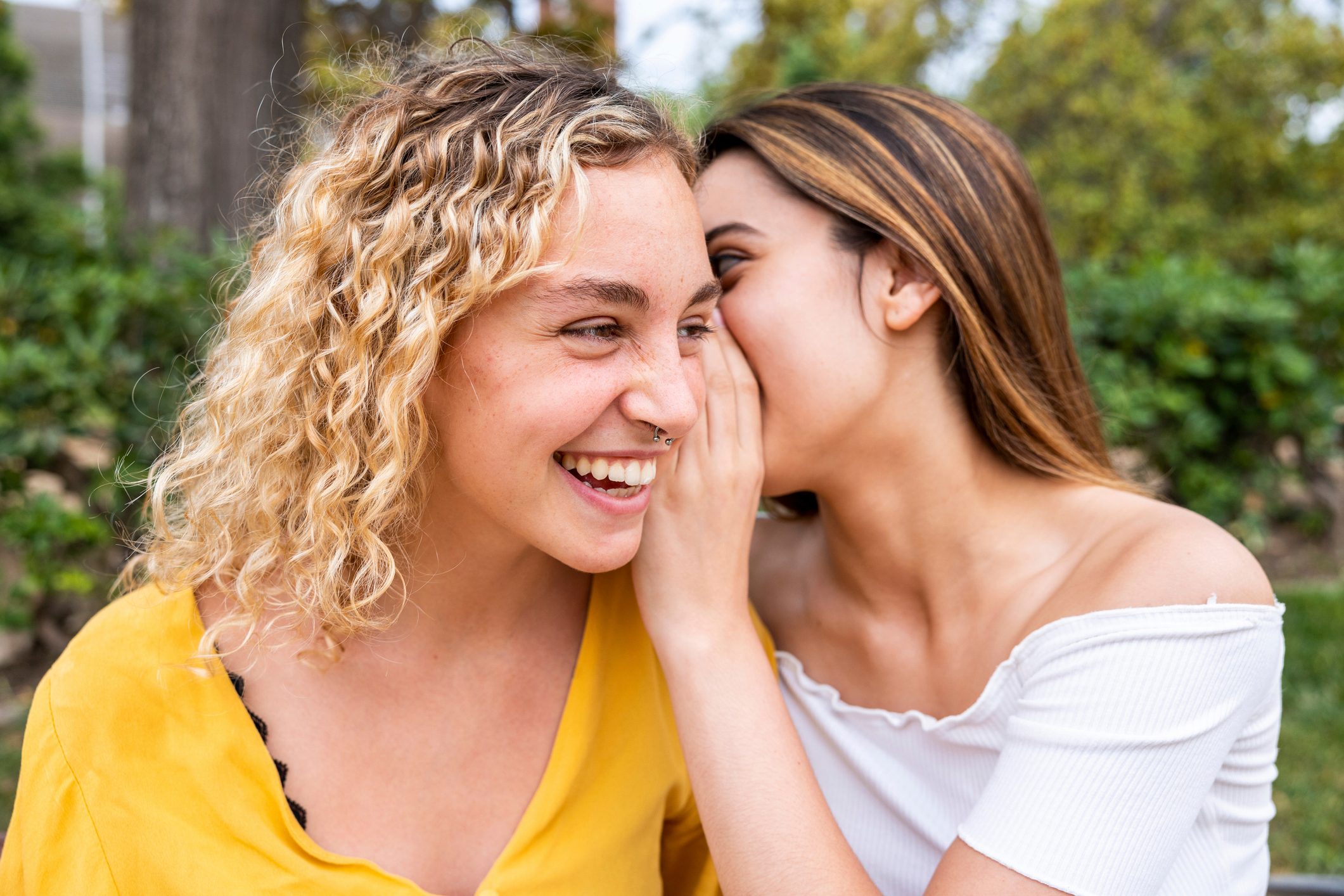 Young woman whispering into friend's ear in park