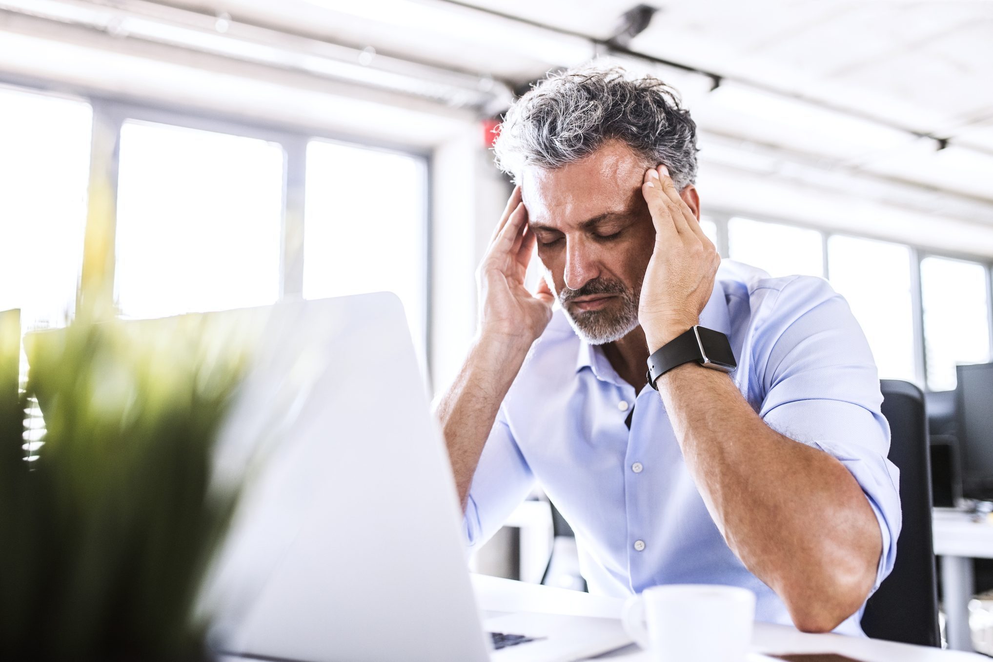 Stressed mature businessman sitting at desk in office with laptop