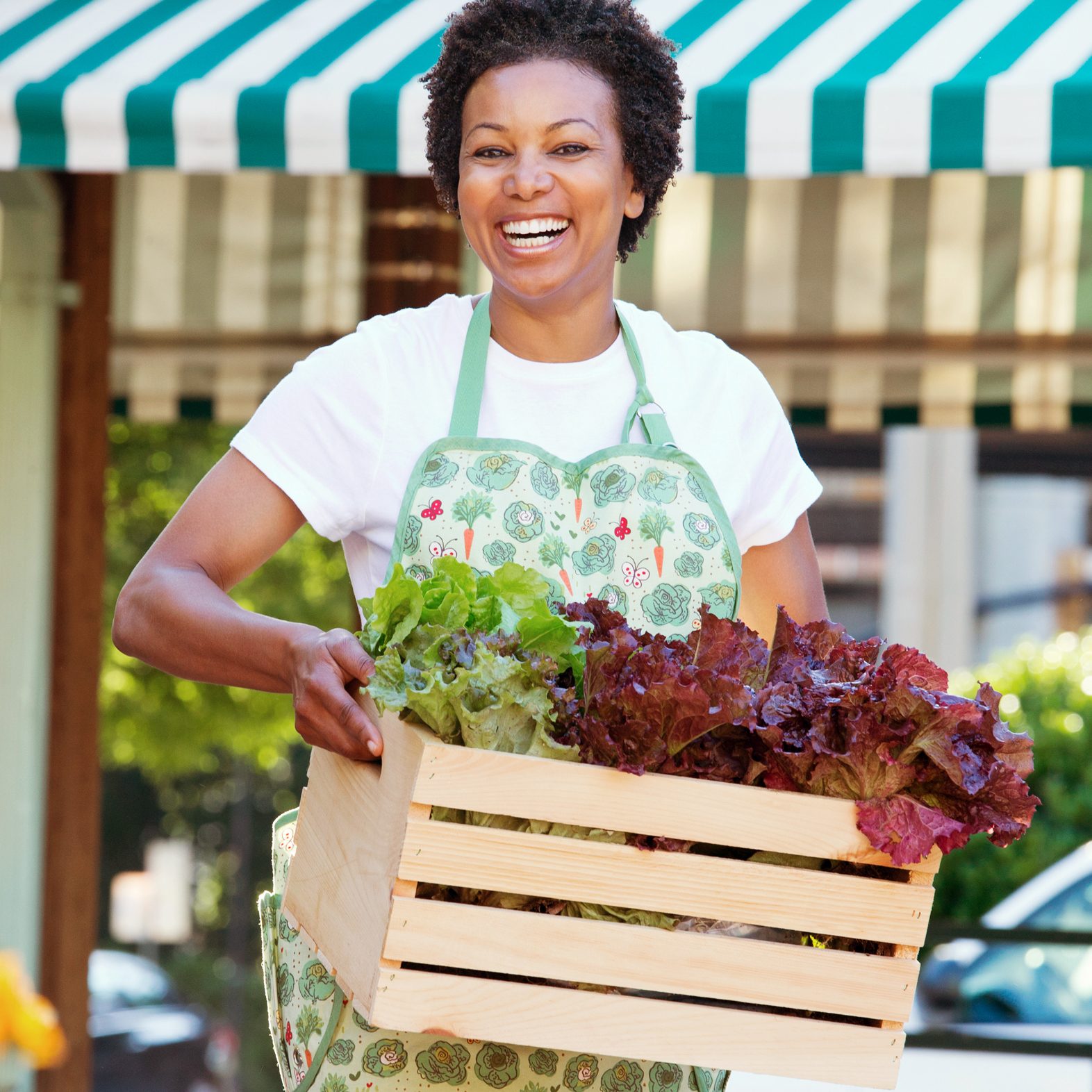 woman carrying wooden crate of lettuce at a farm market