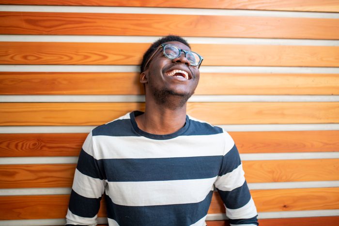 Young Black Man in a striped shirt and glasses Laughing against a wall with a striped wood pattern