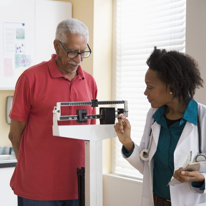 Female doctor weighing senior patient at medical clinic