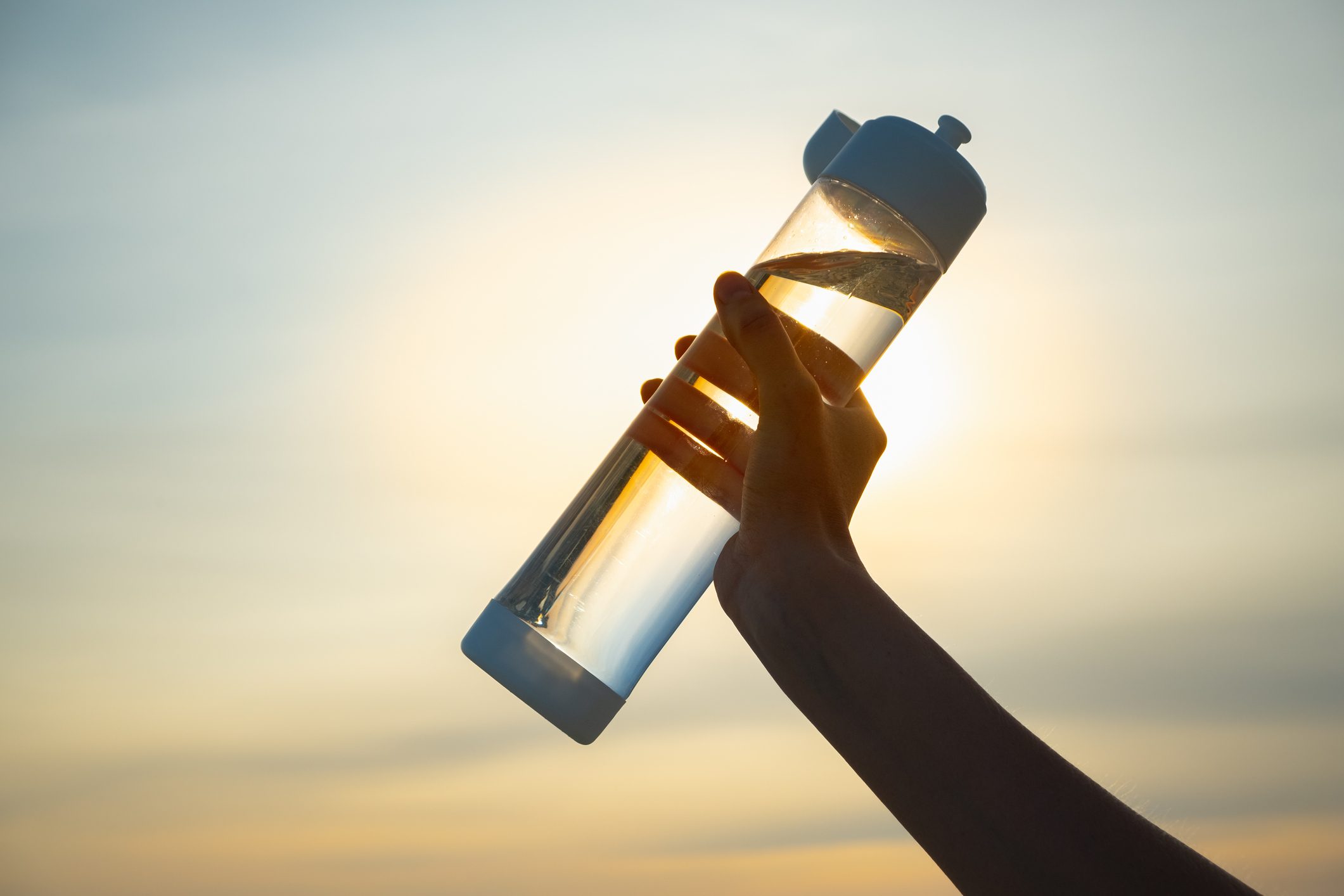 Human hand holds a water bottle against the setting sun.