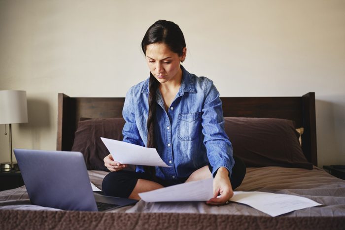 A woman sitting on her bed at home looking at health insurance papers, working with medical matters.
