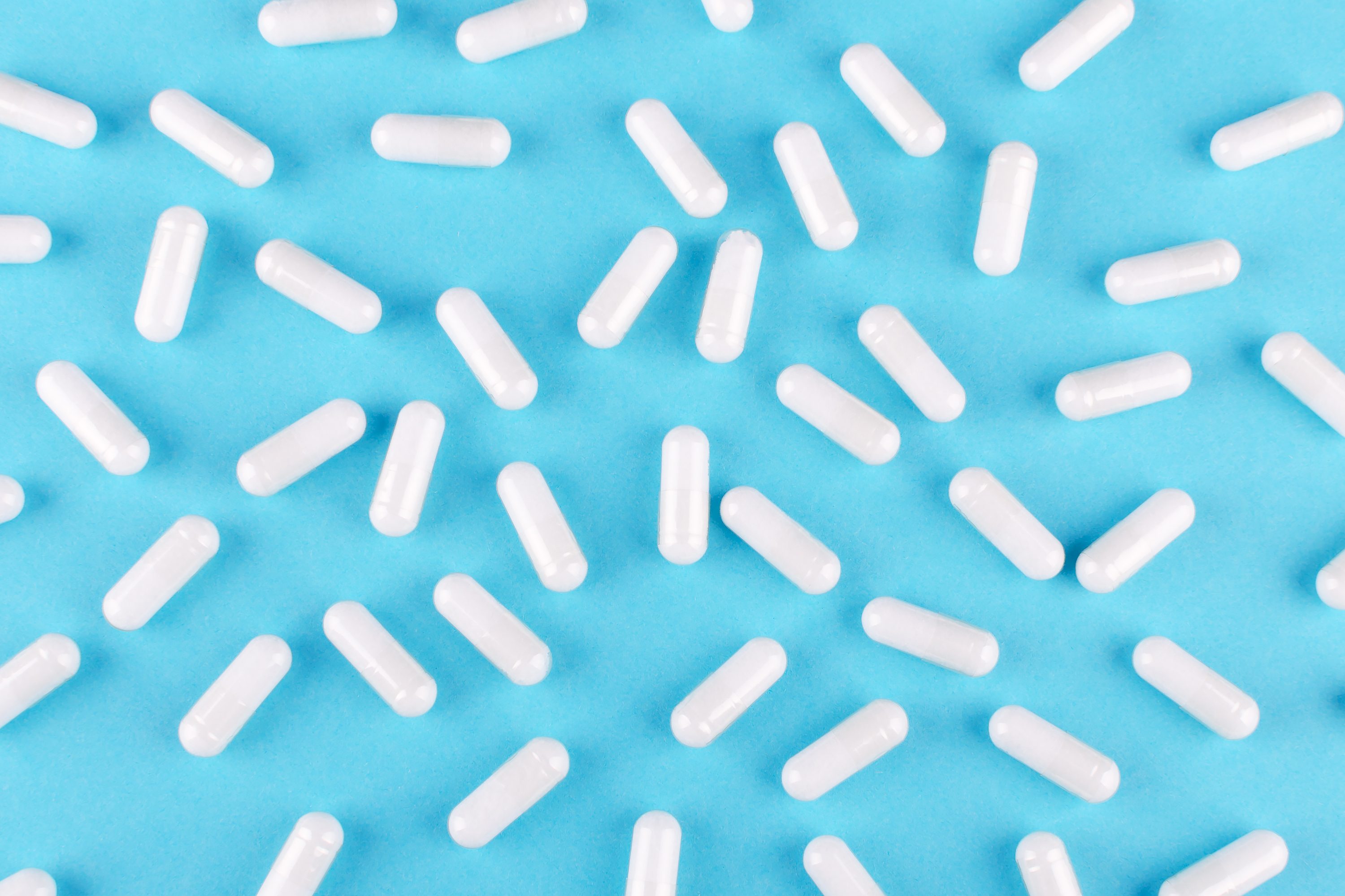 white medicine capsules on blue background, view from above