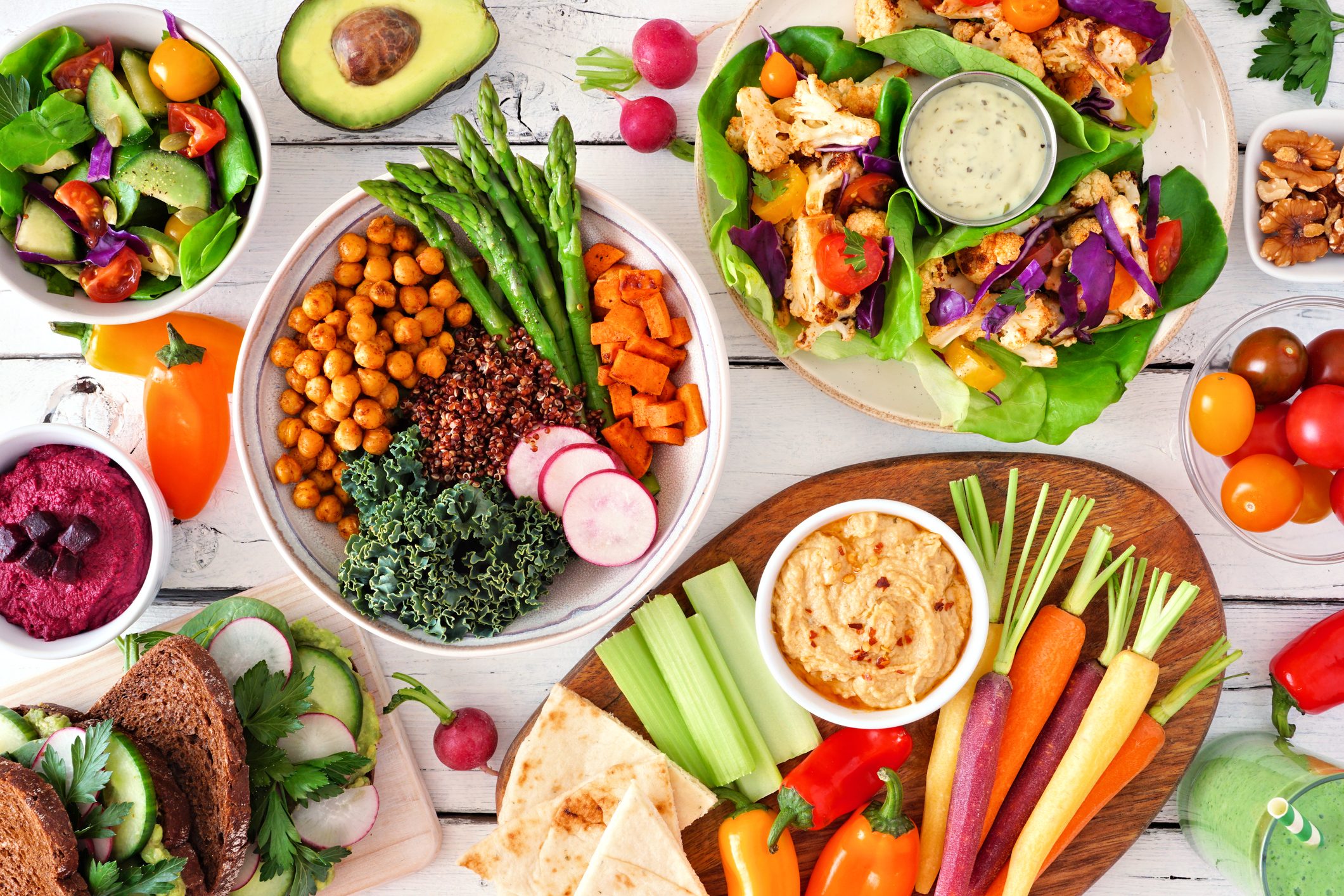 Healthy lunch table scene with nutritious Buddha bowl, lettuce wraps, vegetables, sandwiches and salad, top view over white wood