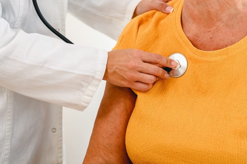 Doctor using stethoscope listening to senior patient wearing a golden yellow shirt