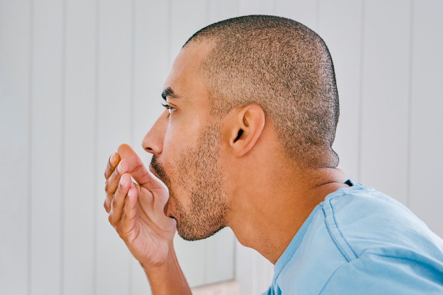 Shot of a young man smelling his breath during his morning grooming routine at home