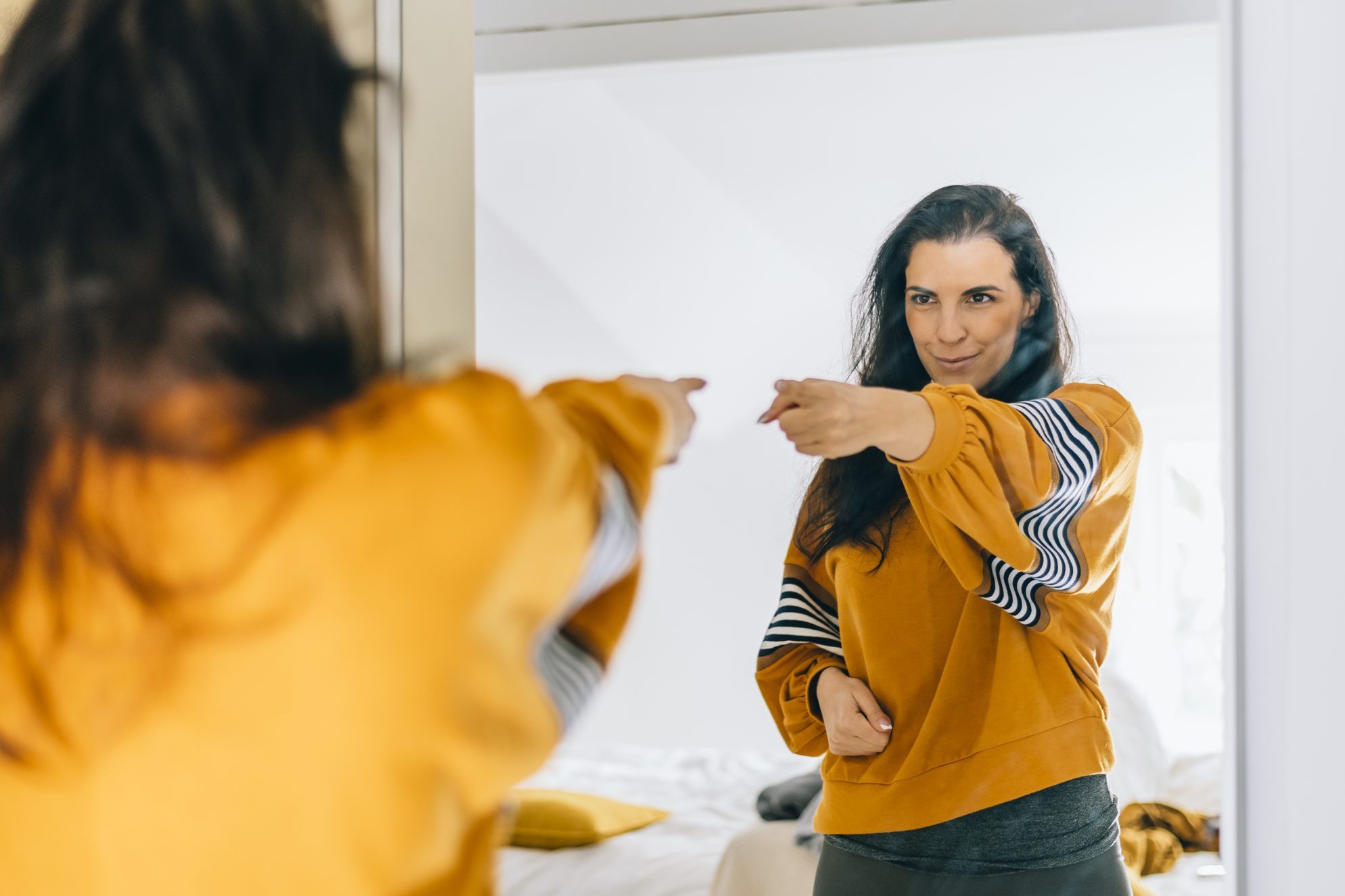 Self confident single woman pointing finger at her reflection in mirror, dancing and felling good