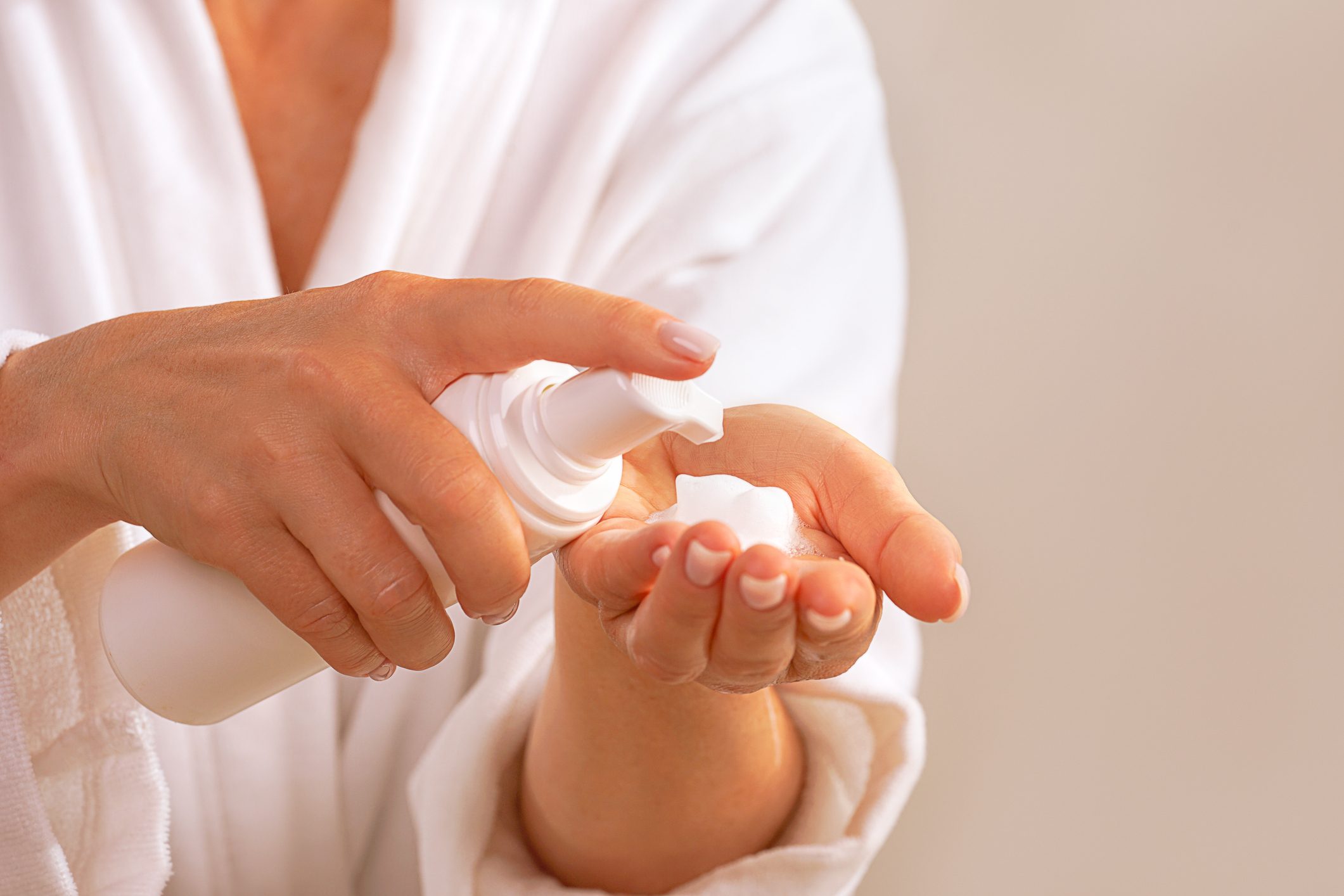 Woman in white bathrobe holds Beauty Product Soap or Cosmetic Milk or Washing Foam.