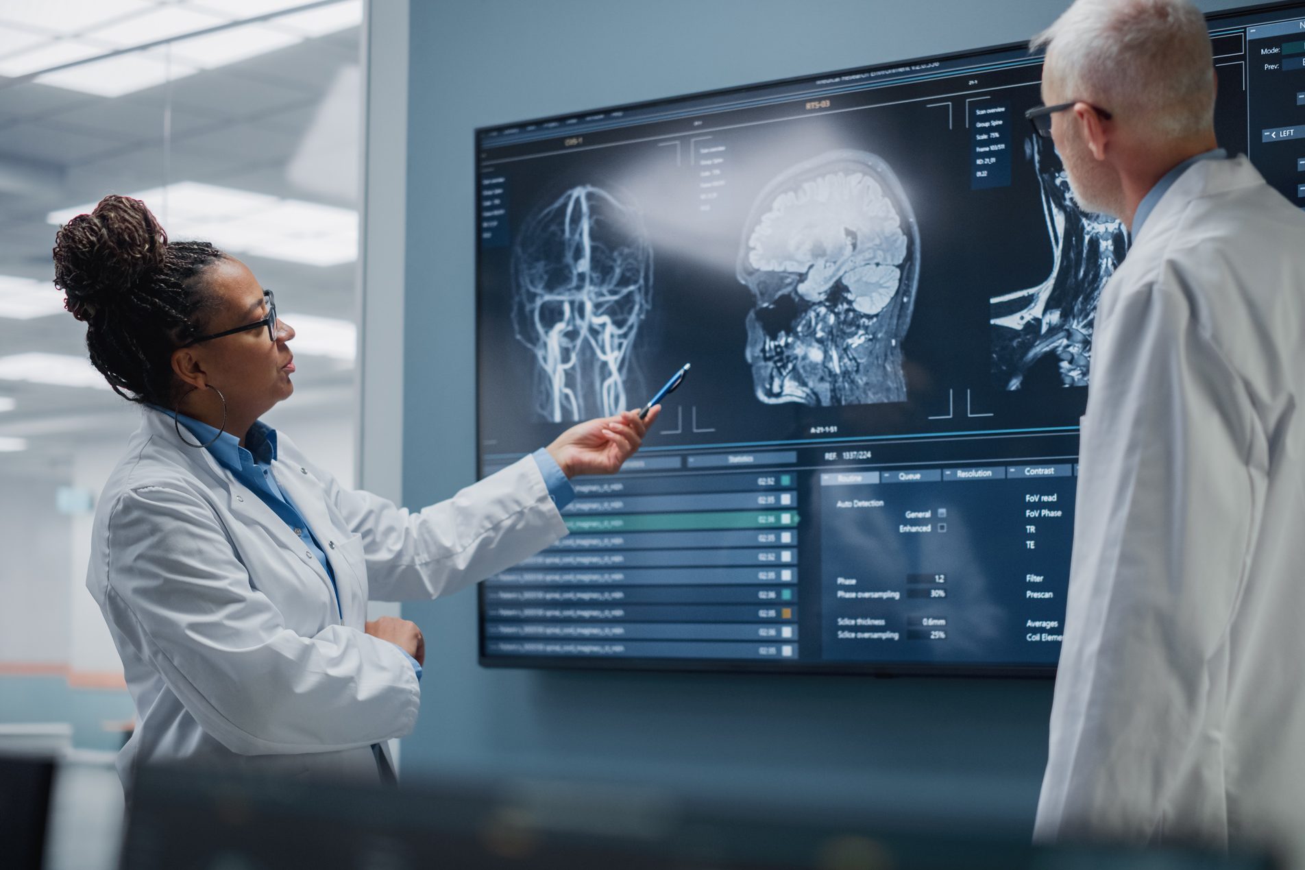 Medical Neuroscience Hospital Lab Meeting: Diverse Team of Neurosurgeon and Neurologist Analyze TV Screen Showing MRI Scan with Brain Images, Talk About Sick Patient Treatment Method, New Drugs Cure