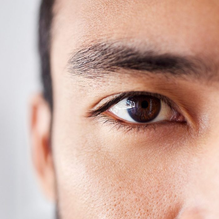 Closeup portrait of a handsome young mixed race man standing at work in an office job. Young hispanic male with naturally long eyelashes and neat eyebrows showing his healthy brown eye