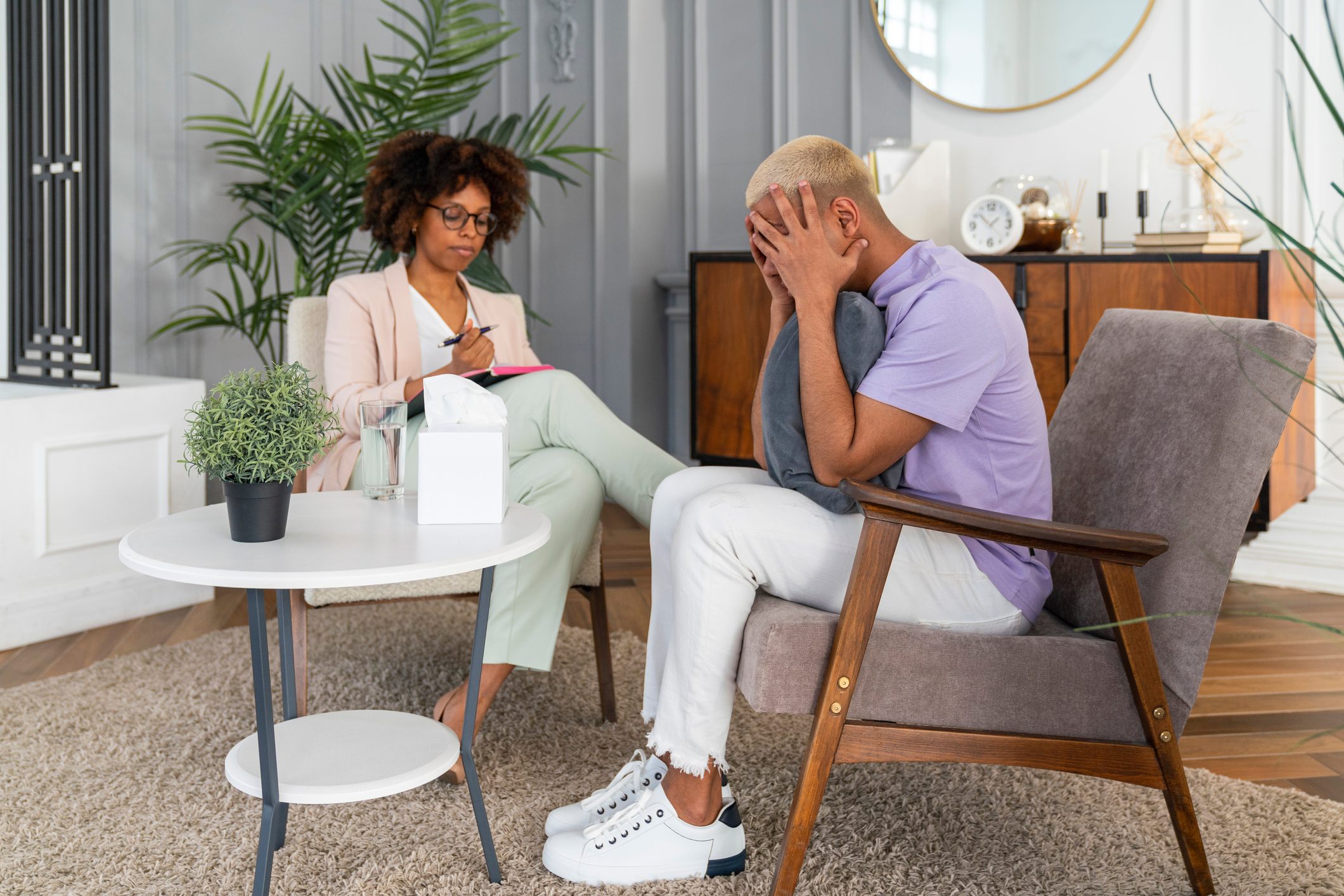 Stressed man with head in hands sitting by psychologist at workplace