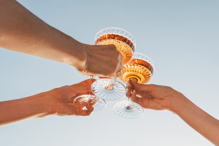 A close-up shot of friends clinking sparkling wine glasses at sunset