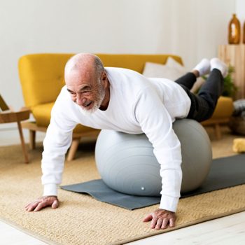 Active senior man exercising on fitness ball at home