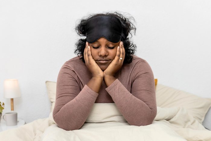 tired woman sitting in bed with an eye mask on her head