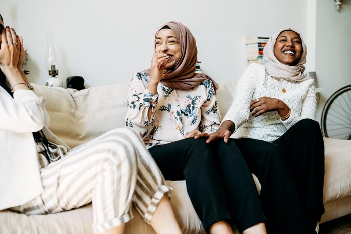 Three friends talking together sitting on the sofa at home