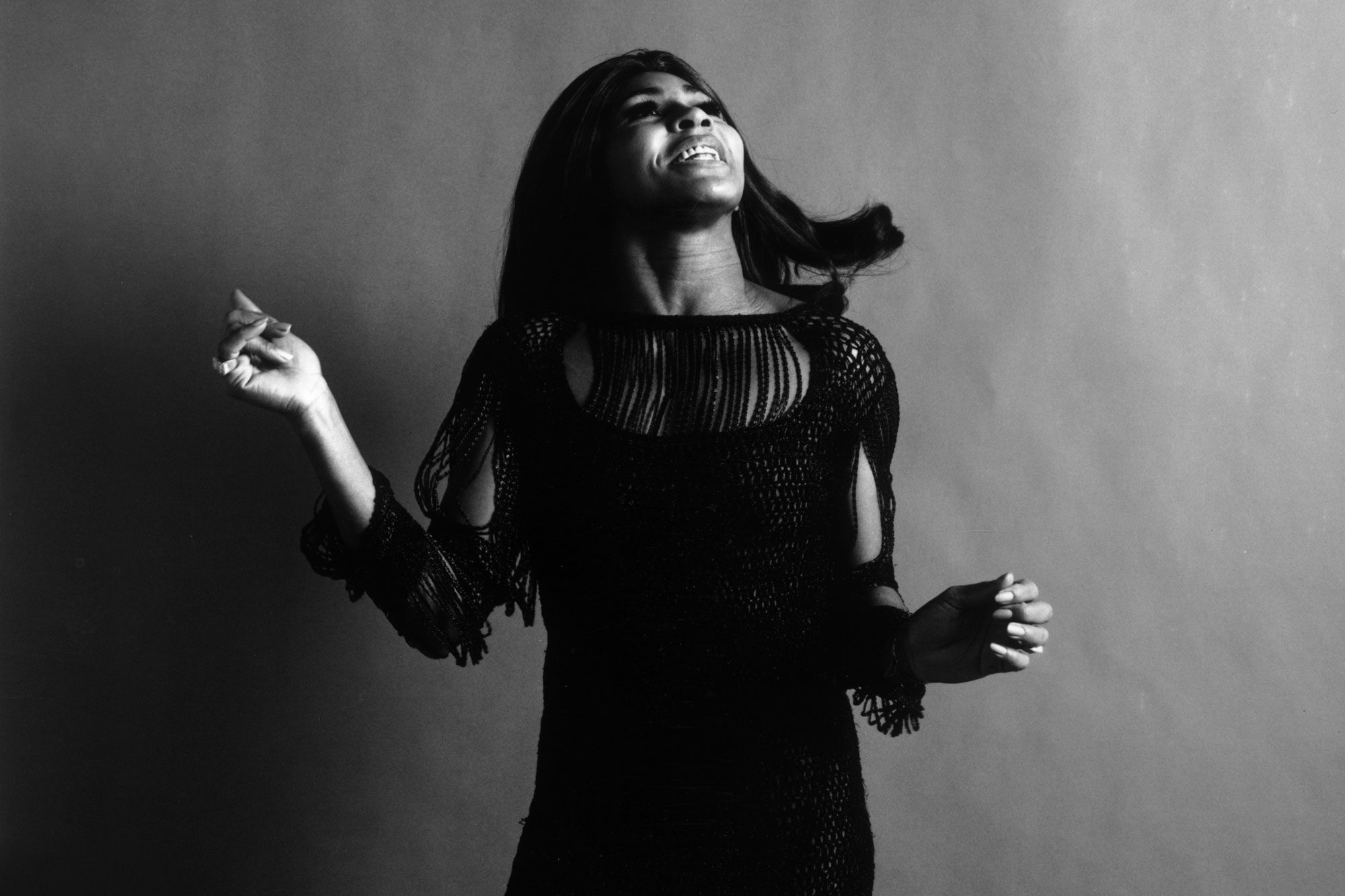 Studio portrait of American rock singer Tina Turner, wearing a dark crocheted mini-dress, looking up and snapping her fingers while singing, New York City, november 1969