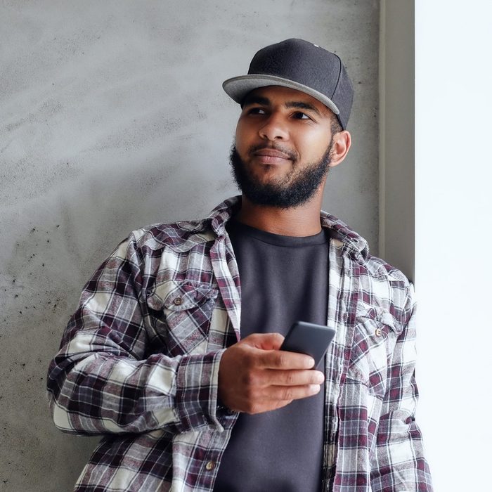 A black male sits near window and using a smartphone.
