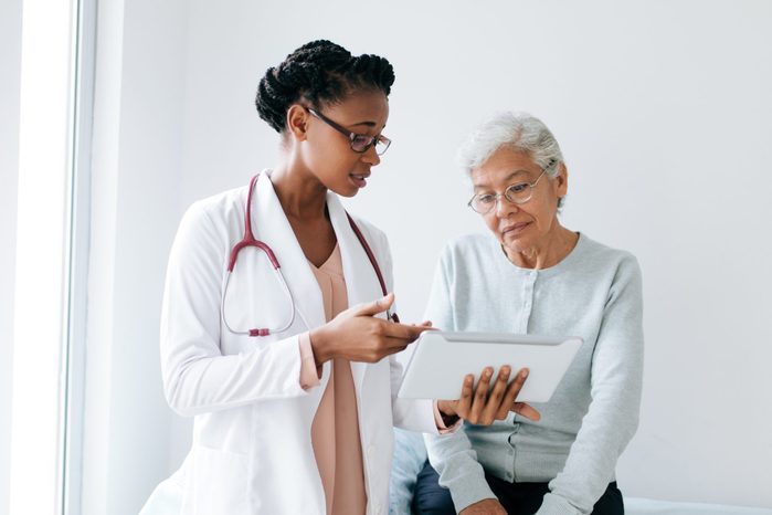 Black female doctor showing digital tablet to senior patient