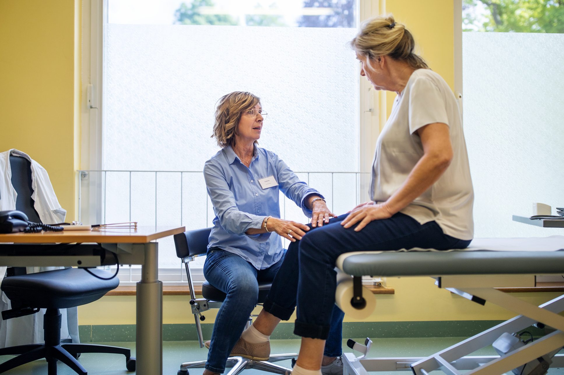 Physiotherapist checking knee of female patient stock