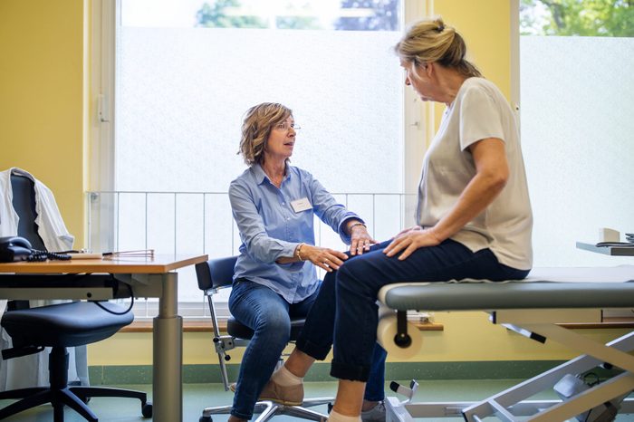 Physiotherapist checking knee of female patient stock