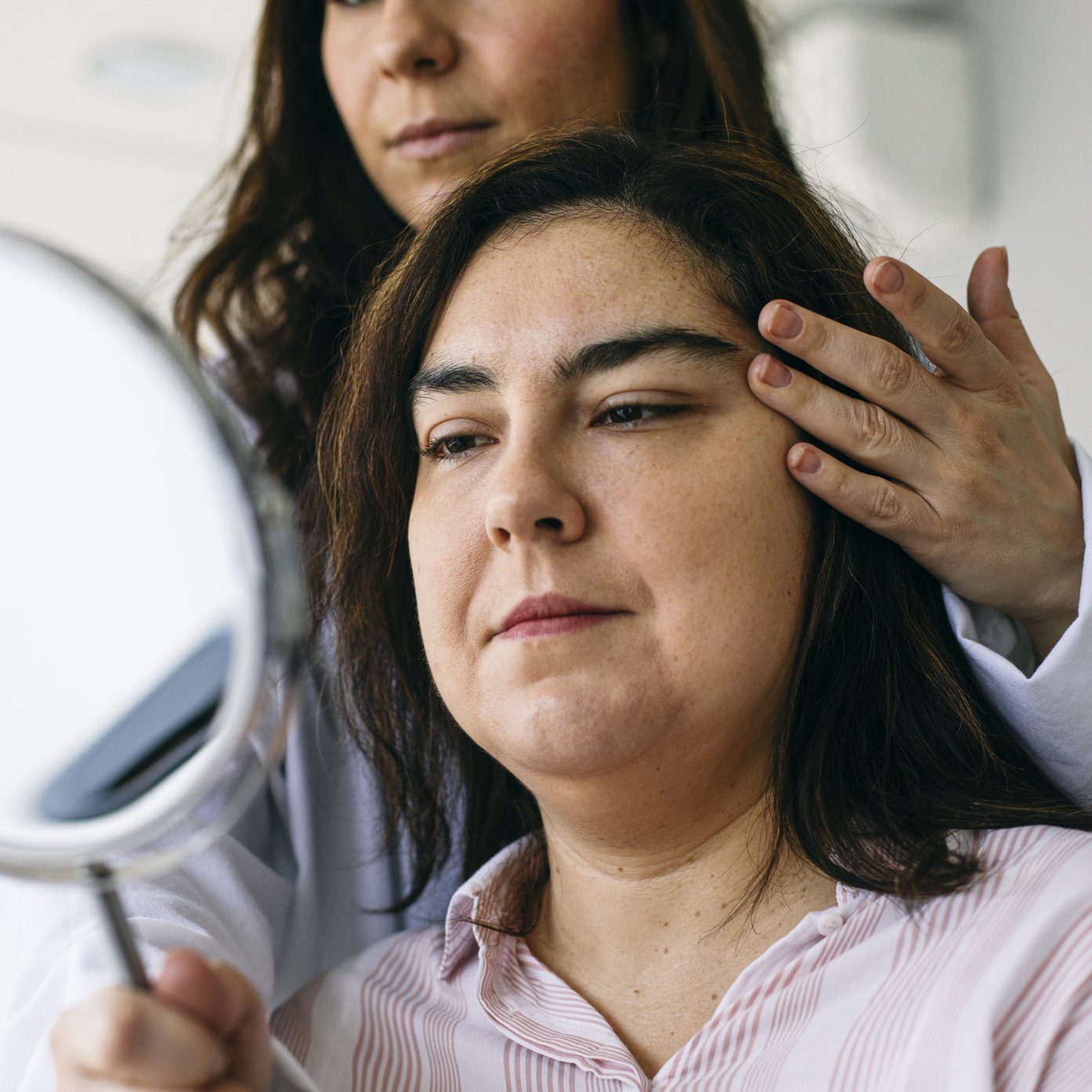 Cosmetic surgeon holding mirror and talking to patient in medical practice