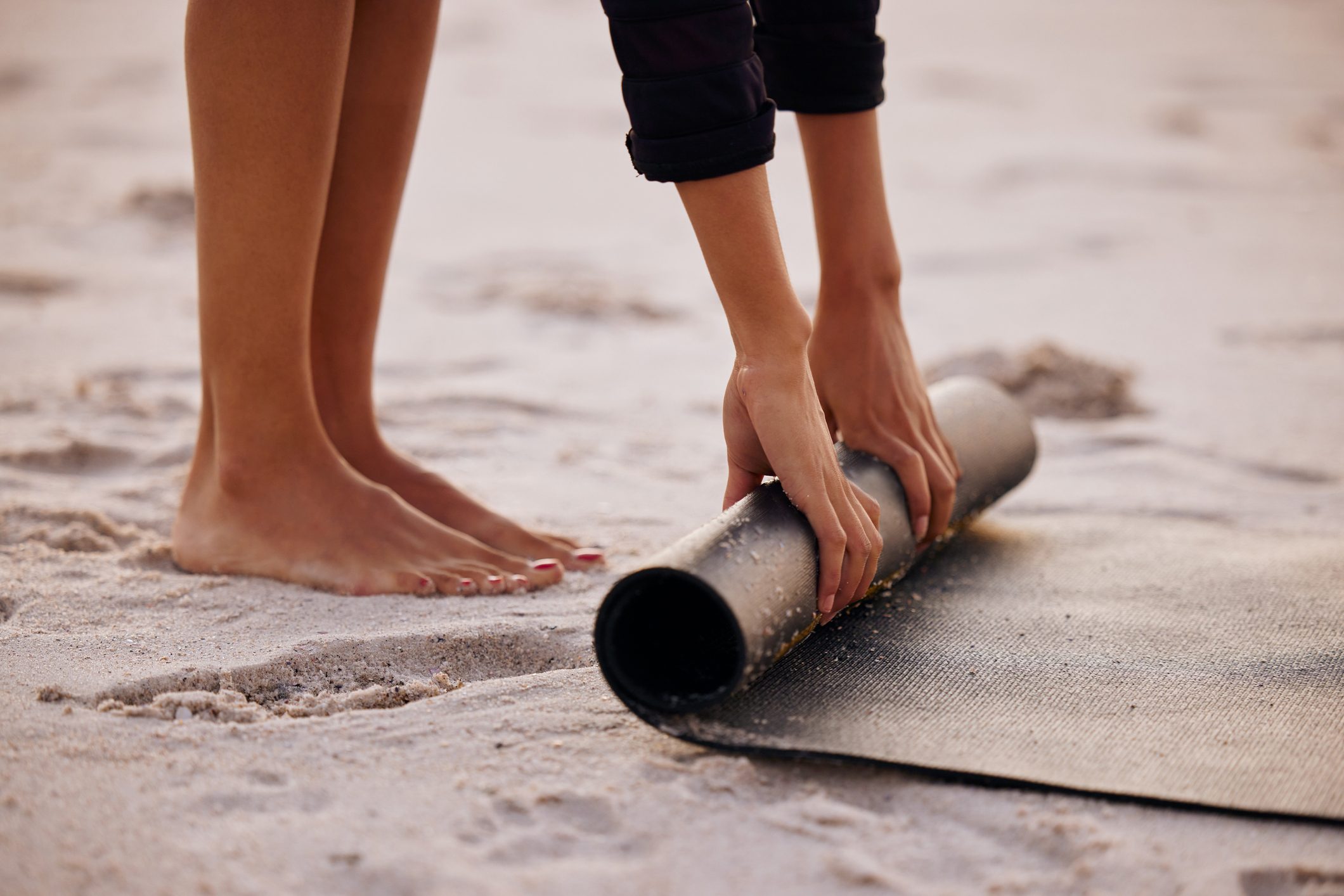 Cropped shot of an unrecognizable woman rolling up her mat after a yoga session on the beach at sunset