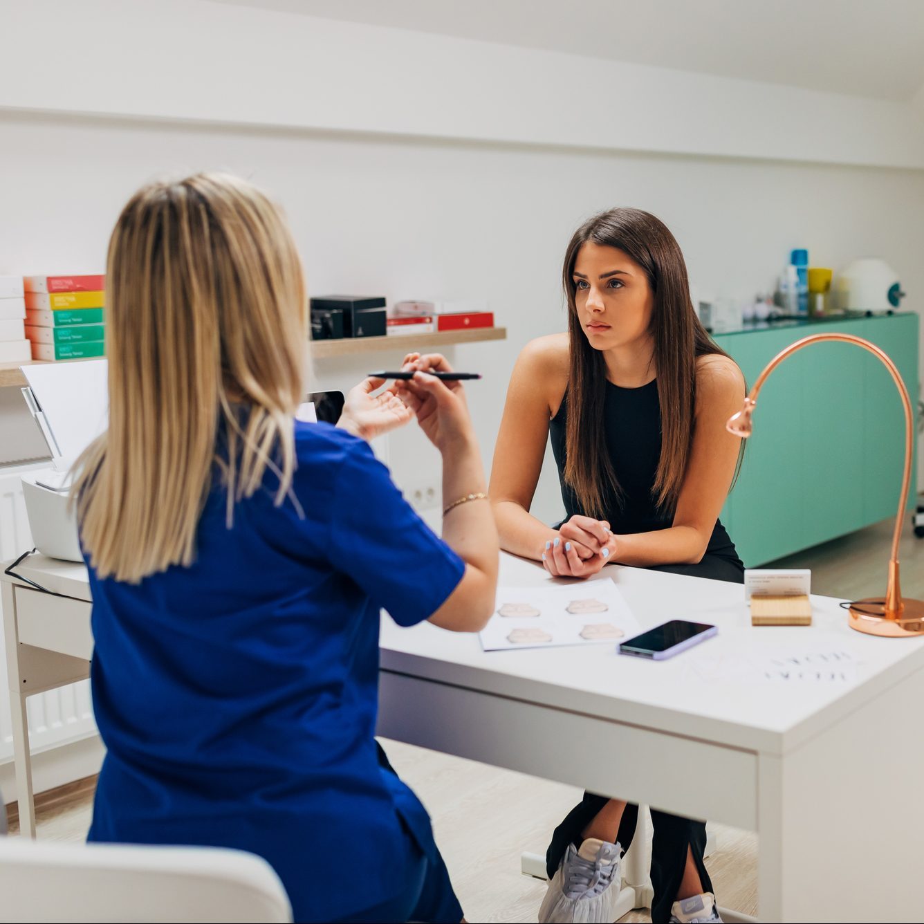Plastic surgeon and patient sitting in doctor's office and talking about medical procedure after plastic surgery