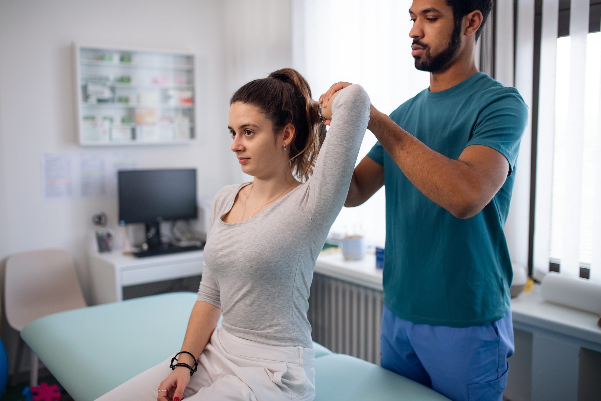 Young male physiotherapist examining young woman patient in a physic room