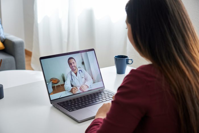 Over-the-shoulder view of a girl sitting at the salon table consulting with her therapist online.