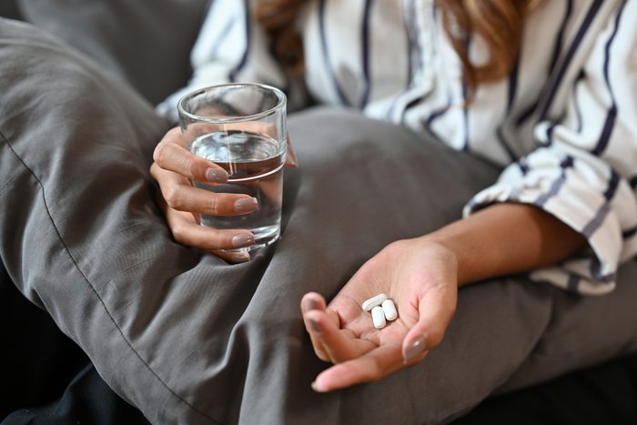 Close up of young female hands holding pack and pills capsules taking medicine for relieving female period. Health care and nutrition concept.